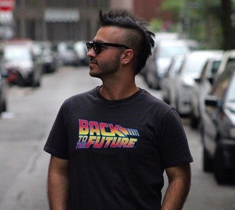 Best hair styling products for men guide: Close up shot of a man with medium, dark brown hair styled into a mohawk, wearing a top and posing in the street.