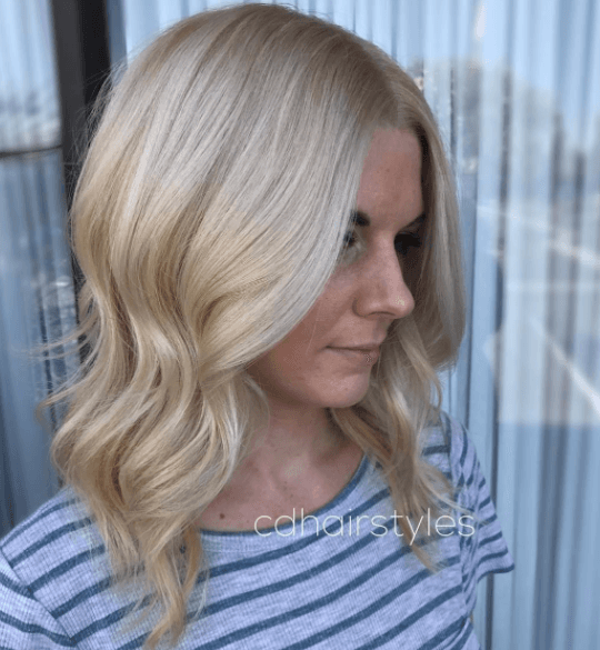 side view of a woman with shoulder length wavy hair and an all over blonde colour