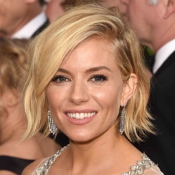 wavy blonde bob on Sienna Miller wearing a white and silver dress with droplet earrings in the red carpet