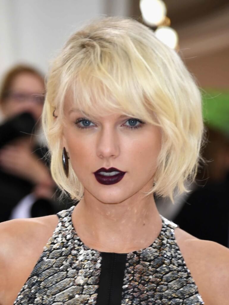 Taylor Swift with a wavy bleach blonde bob with side fringe wearing dark lipstick