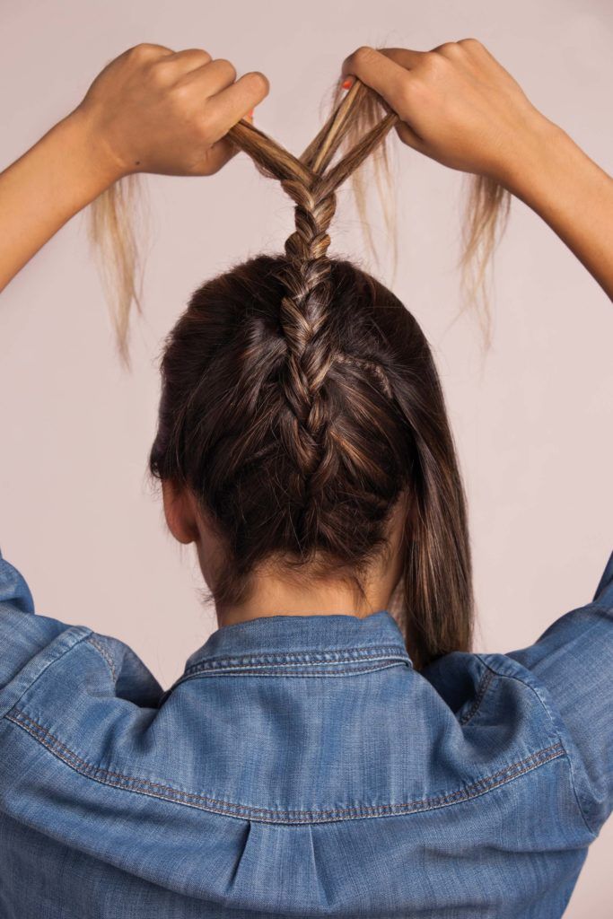 How to do a braided top knots: blonde woman braiding wavy hair wearing a denim shirt
