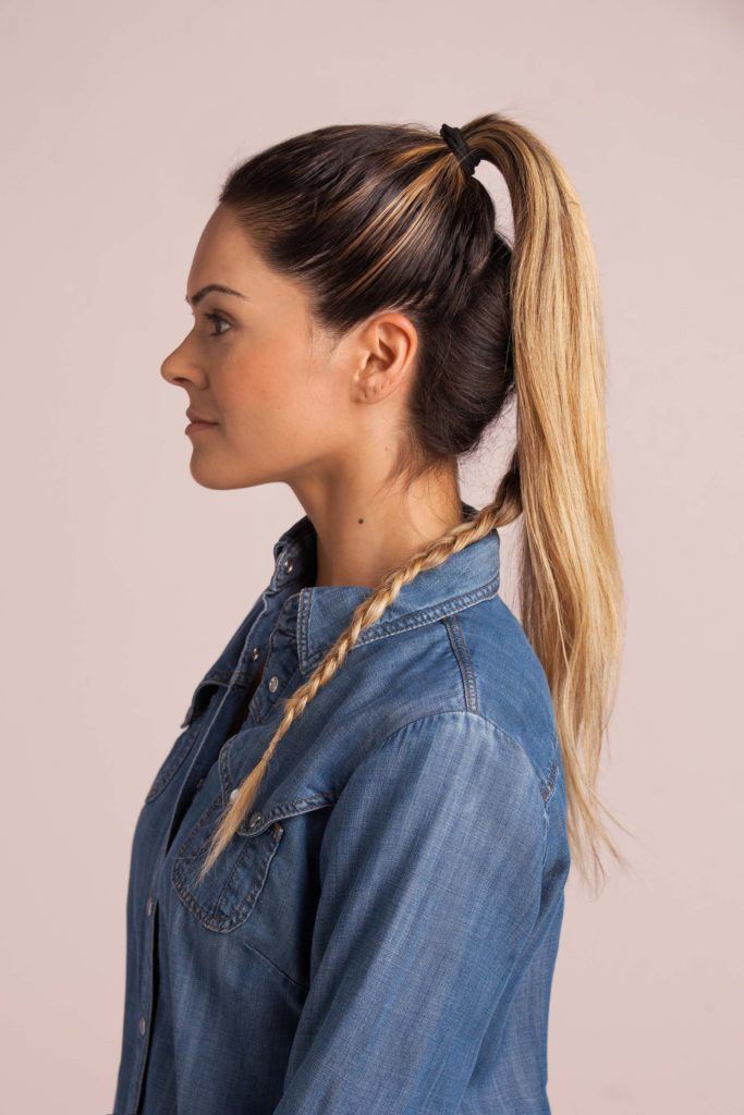 braid top knot: blonde woman with a braid at the bottom and holding half her hair into a high ponytail wearing a denim shirt