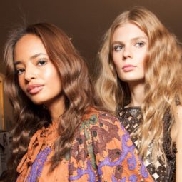 Wavy Hair Products: two models backstage one brunette and one blonde both with long wavy hair