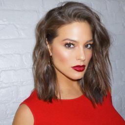 Ashley Graham with short wavy bob hair with a red top and red lipstick