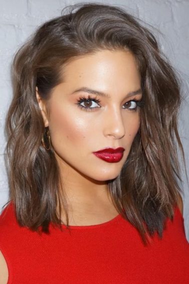 Ashley Graham with short wavy bob hair with a red top and red lipstick