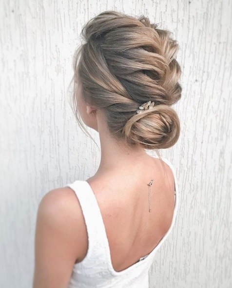 Wedding hairstyles for long hair: Woman with light brown/dark blonde hair in a French braid into a chignon bun