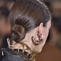 bun hairstyles: model with medium brown hair styled in a wet look low twisted bun hairstyle with large gold earrings and necklace