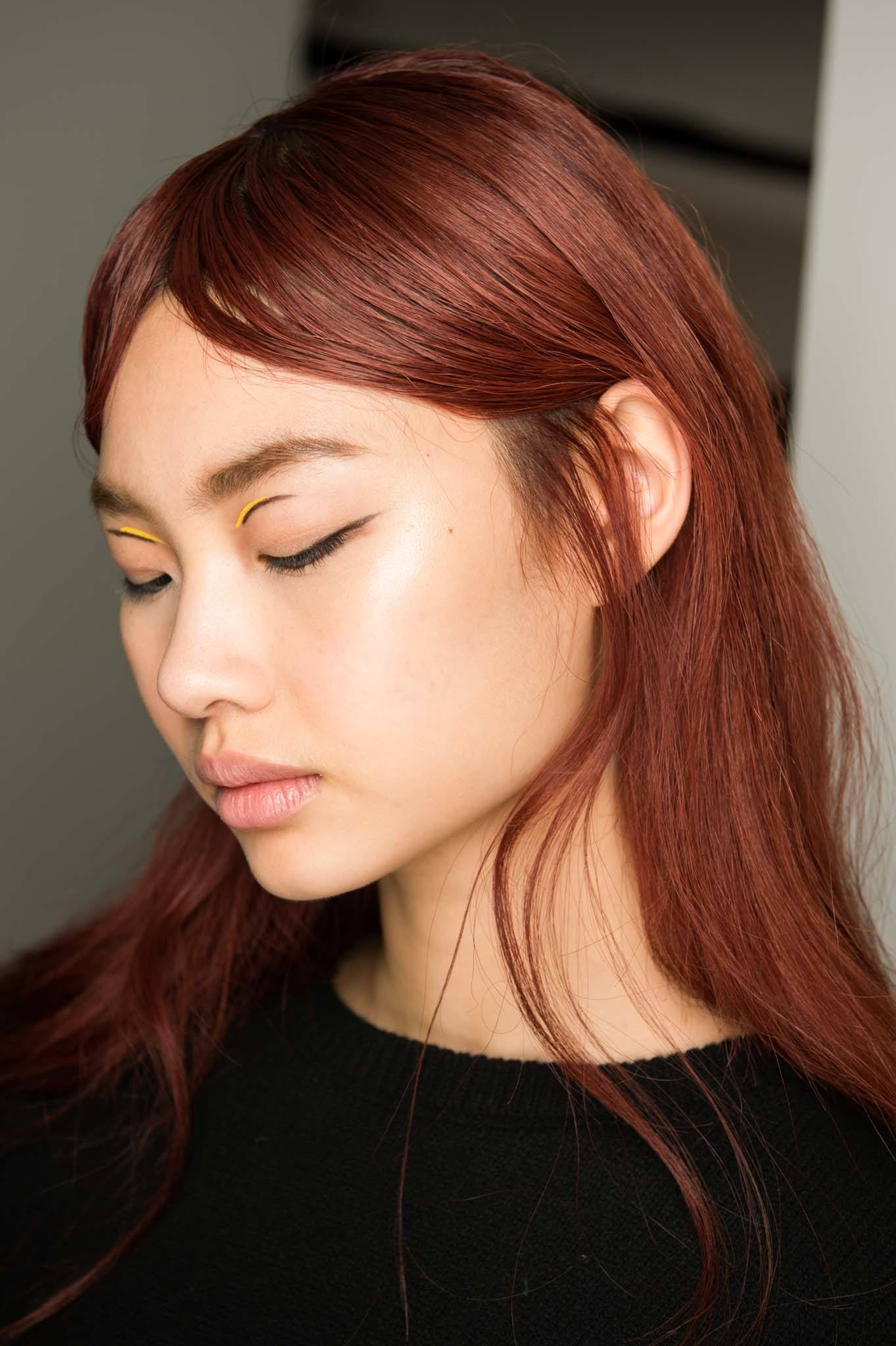 Hair glossing treatment: Woman with rich red straight hair looking down wearing a black top.