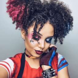 Woman dressed as Harley Quinn with curly natural hair in pigtails with pink and blue chalked ends