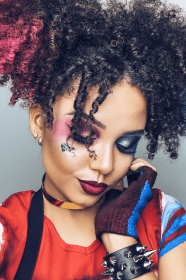 Woman dressed as Harley Quinn with curly natural hair in pigtails with pink and blue chalked ends