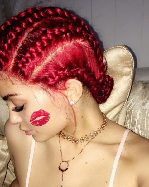 Kylie Jenner's red hair with cornrows posing to the side with a kiss of red lipstick on her cheek