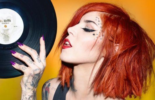 kat von d with dyed red hair holding a vinyl record with purple nails and stars on her face