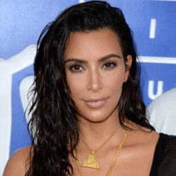 Kim Kardashian on the red carpet at the VMAs wearing a sheer black outfit and gold necklaces with her long dark brown hair worn in waves and a wet look style