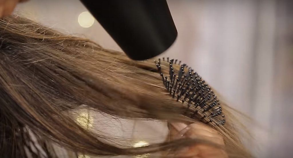 Gibson girl hair tutorial: Close-up of brunette hair being blow dried with a paddle brush