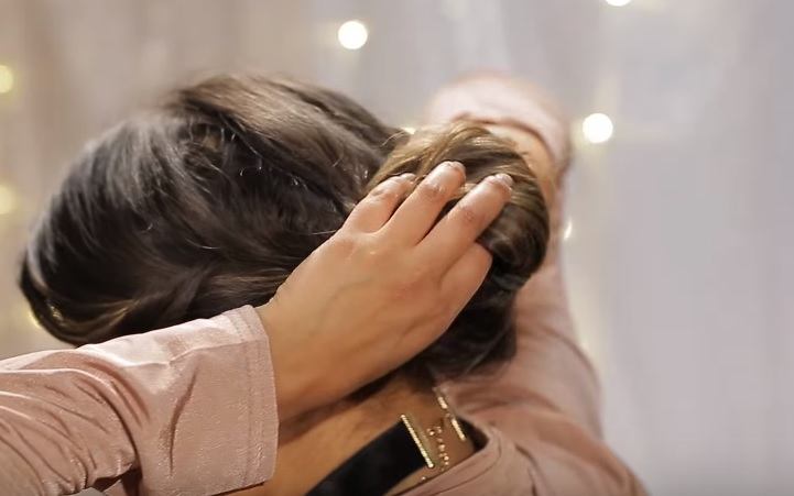 Gibson girl hair tutorial: Back view of a woman with brunette hair rolling her ponytail up into a chignon