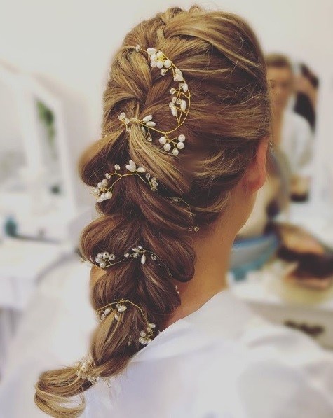 Wedding hairstyles for long hair: Back view of a woman with golden brown hair in a voluminous pull through braid accessorised with small flowers