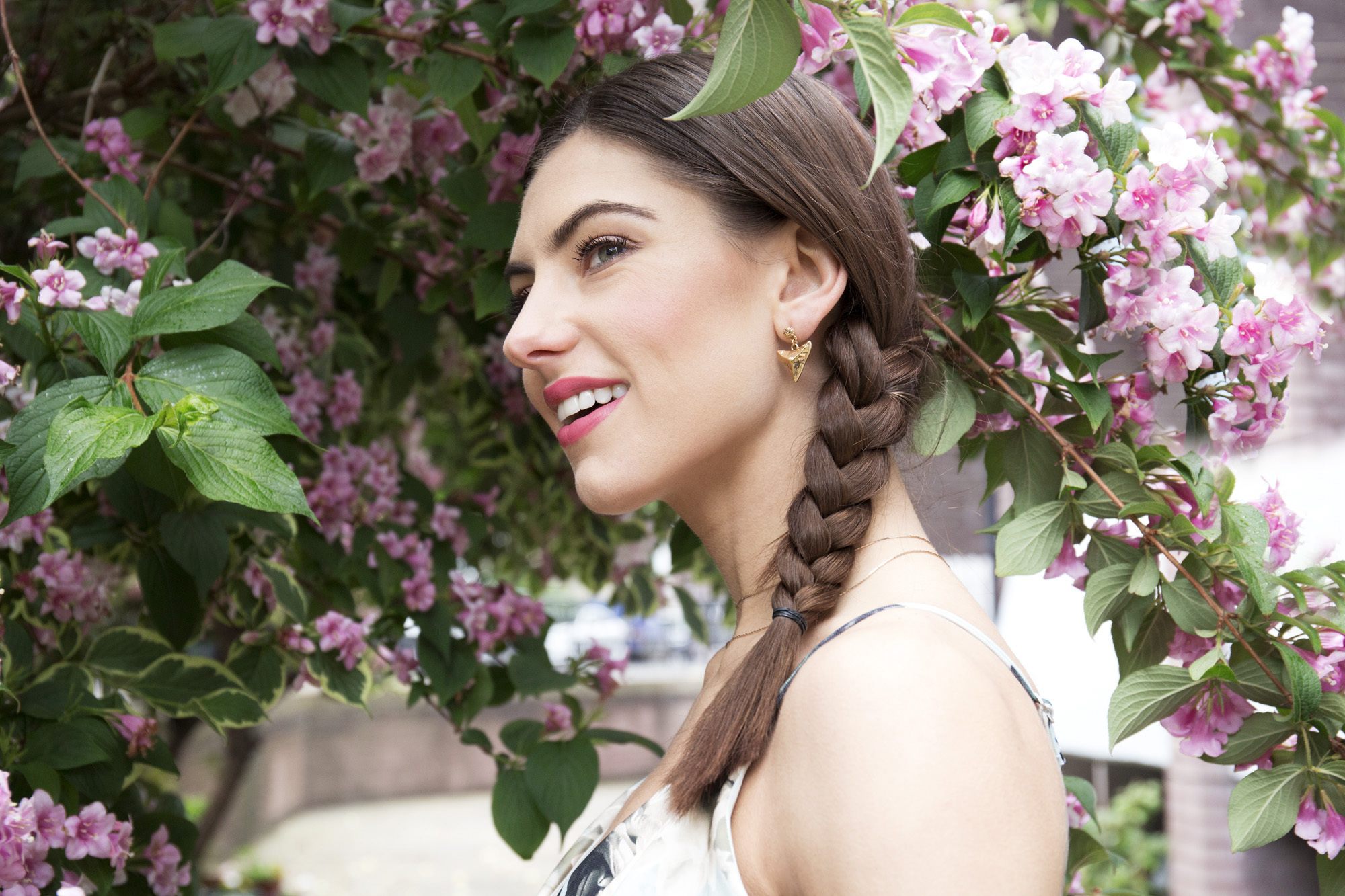 brunette model with three strand side braid under a tree with flowers