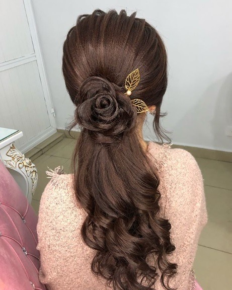 Wedding hairstyles for long hair: Back view of a woman with long curled chestut brown hair with a floral rose braid detail and a gold leaf clip
