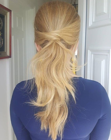 Wedding hairstyles for long hair: Back view of a blonde woman with her hair in a wrapped textured low ponytail
