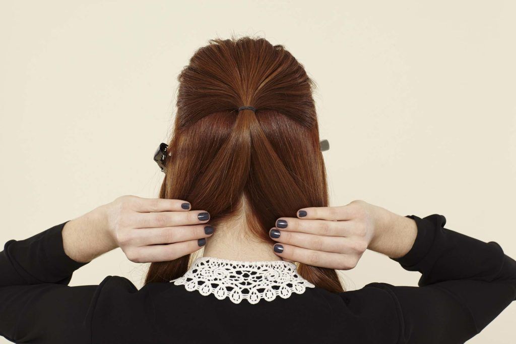 The back view of redheaded model parting half-up ponytail into two for a twist updo