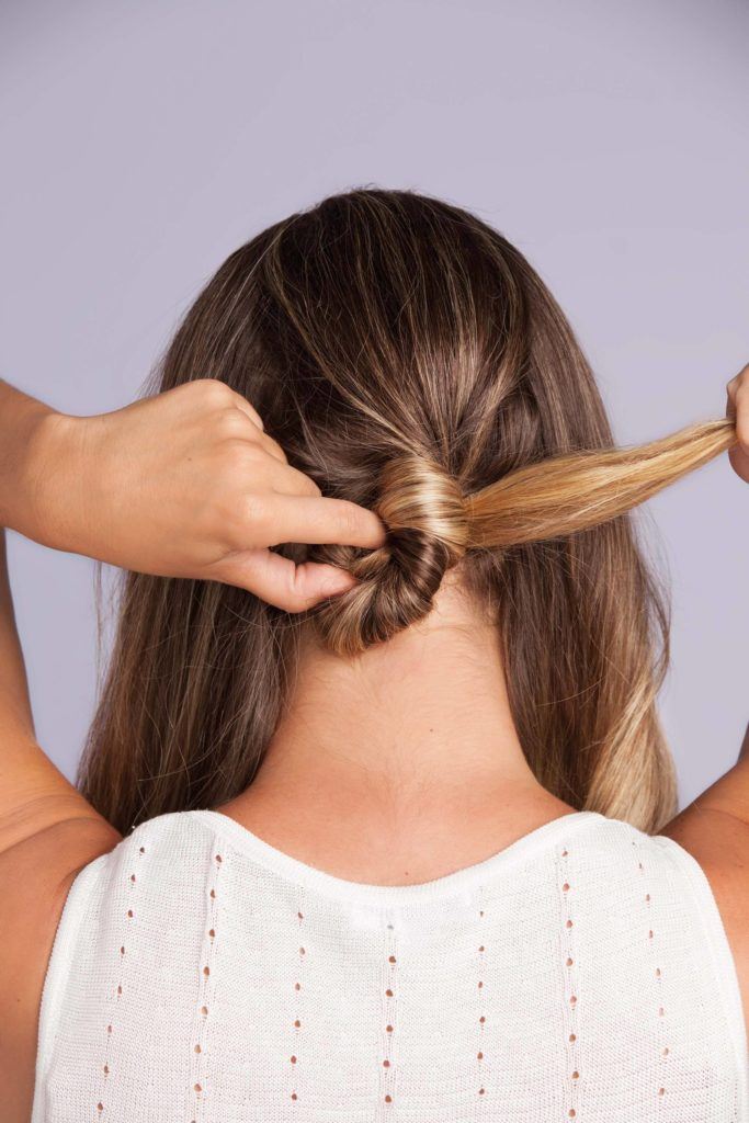 a woman tying up her long blonde hair