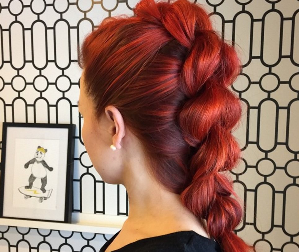 back view image of a woman with bright red bold hair in a French braid faux hawk
