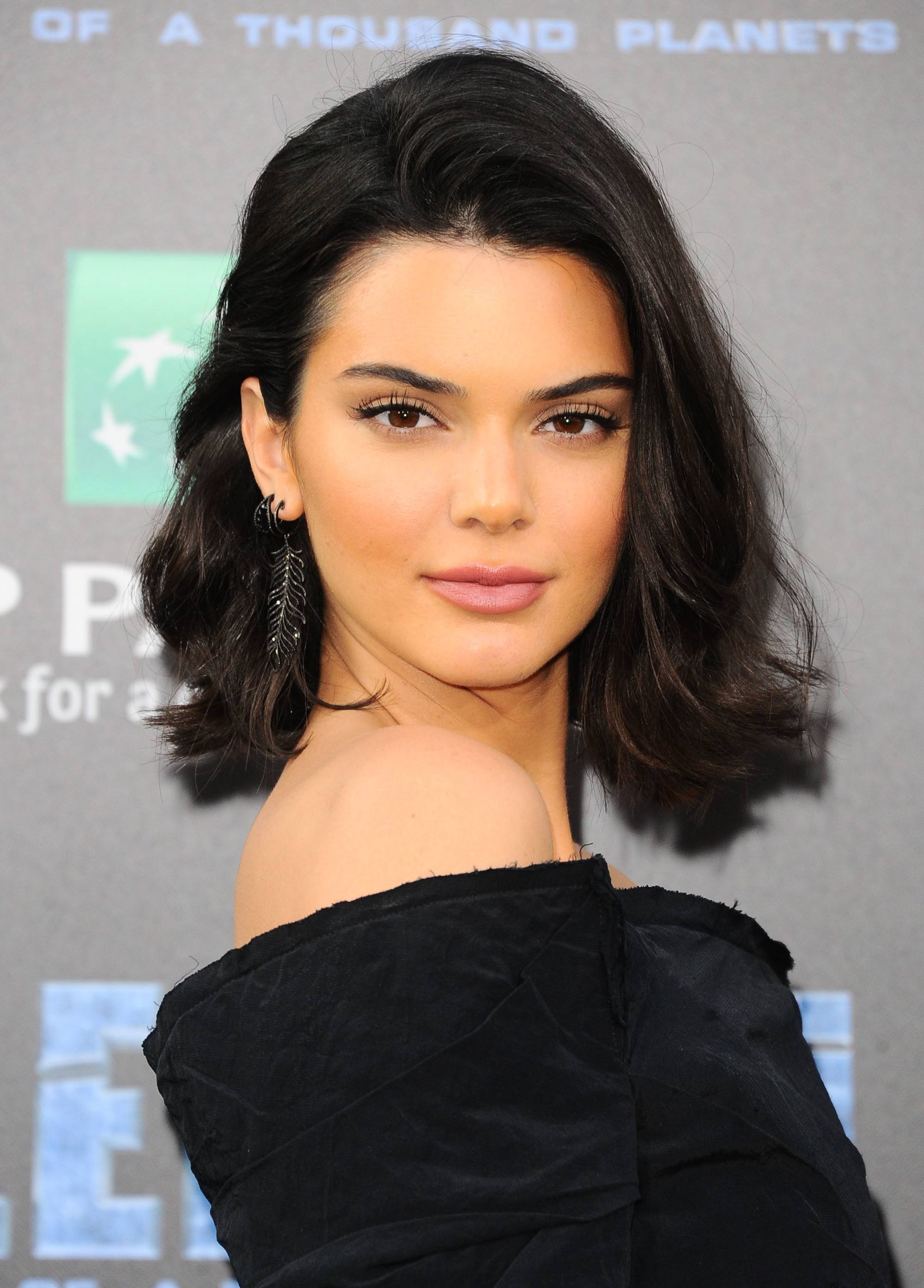 Medium hairstyles for thick hair: Kendall Jenner with dark brown long bob length hair with flicked-out layers, wearing an off shoulder black dress