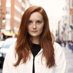 Red hair: Woman on the street with long pumpkin spice hair with side parting wearing a white jacket over a black top.
