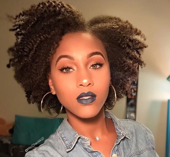 close up shot of woman with side part afro hairstyle, wearing blue lipstick and hoop earrings and denim jacket