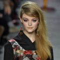 blonde model with long hair in deep side parting with sweeping fringe wearing dark floral pattern dress at runway show