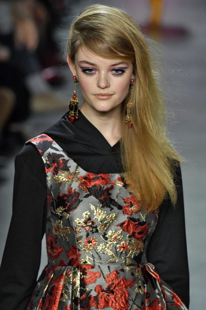 blonde model with long hair in deep side parting with sweeping fringe wearing dark floral pattern dress at runway show