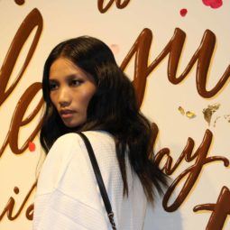 model backstage at the Rebecca Minkoff SS17 show wit dark brunette hair in waves wearing a white outfit and a black strap bag