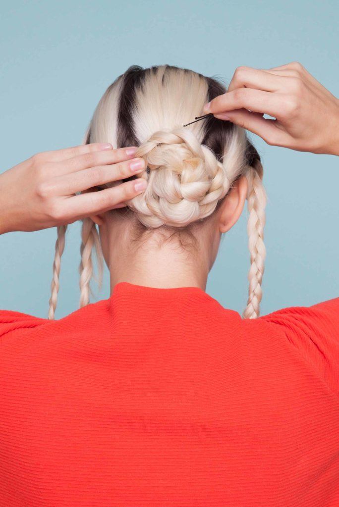Snake braid hairstyles: Back view of woman with blonde hair finishing a snake braid hairstyle by adding bobby pins.