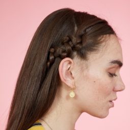 Snake braid hairstyles: Side view of brunette woman with long straight hair styled with snake braid. Picture taken in a studio with pink background. Model is wearing a yellow striped dress.