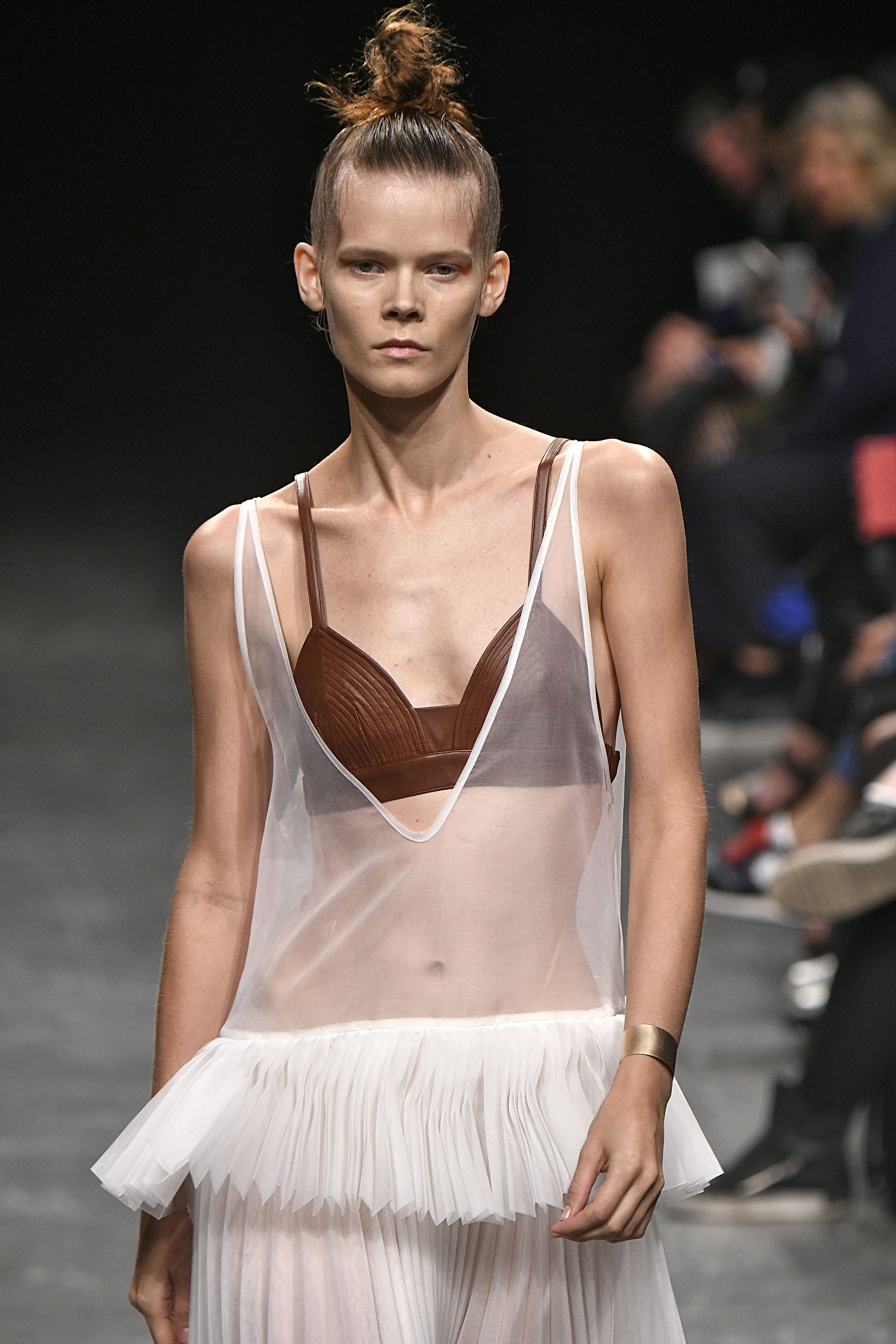 close up shot of model on the wunderkind runway with sleek top knot, wearing transparent top and tulle dress and walking on the runway