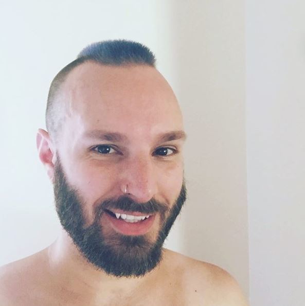 Dark haired man with beard and subtle, barely-there mohawk