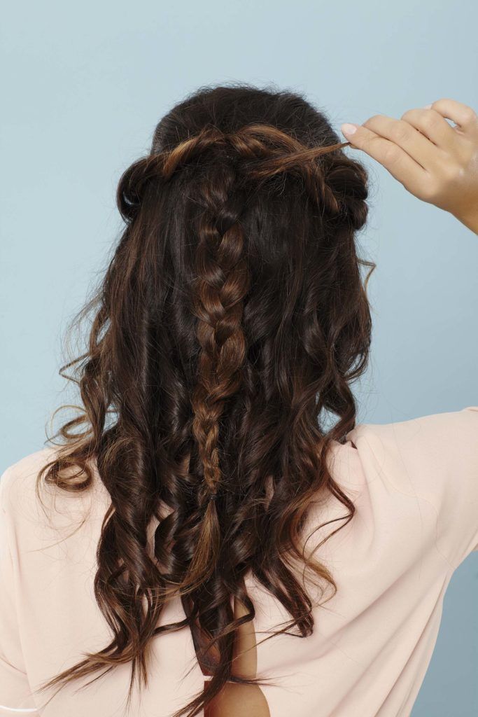 back shot of a woman with long brunette hair adding extra hair into her braid