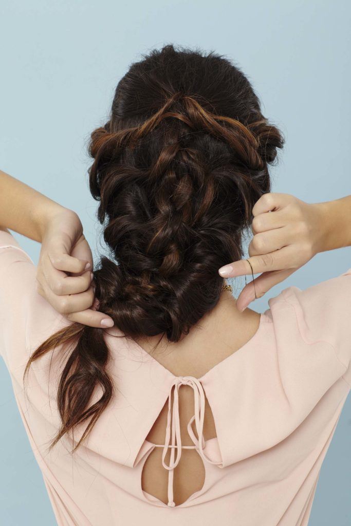 back shot of a woman with long brunette hair securing her braid with a hairband