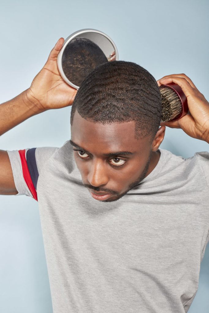 360 waves: Man with 360 waves and facial hair wearing a grey t-shirt, using a mirror to brush the back of his hair