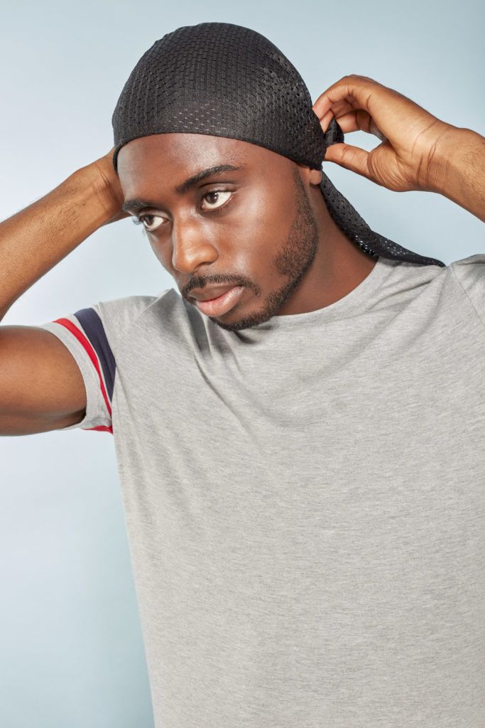 360 waves: Man tying a black silky durag around his short afro hair, wearing a grey t-shirt