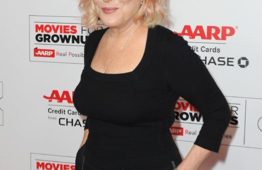 Bette Midler on the red carpet wearing black top and navy spriped trousers with her hair worn in a blonde bob cut with pink highlights