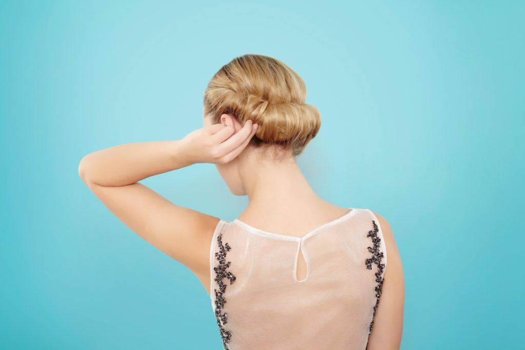 back view of a blonde model twisting her hair into a croissant chignon updo