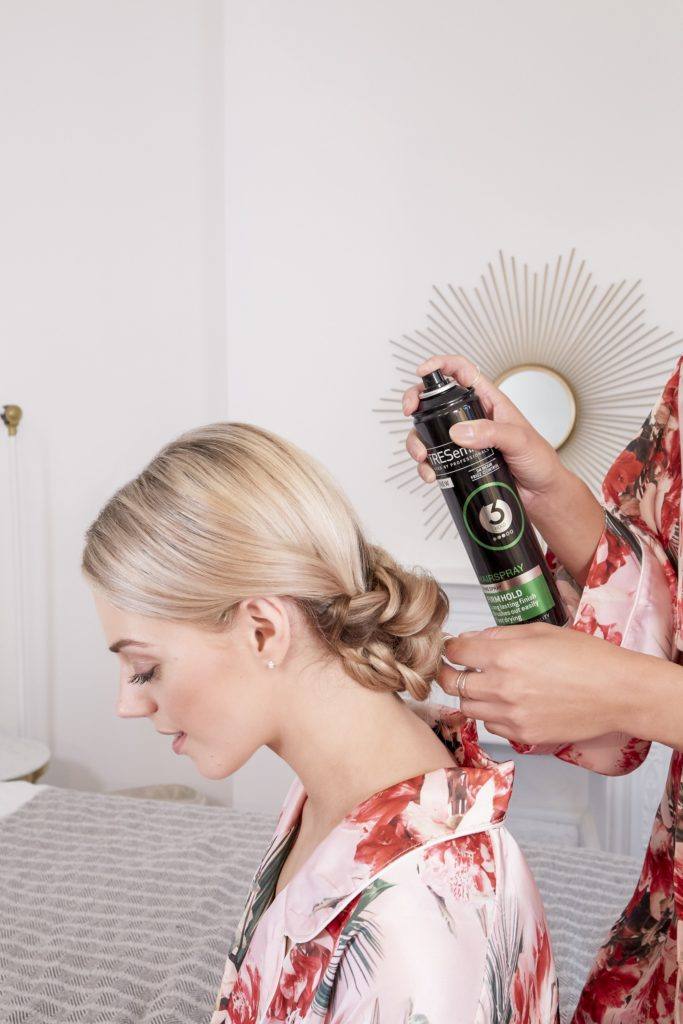 wedding chignon: blonde model with a braided wedding chignon having her hair sprayed with tresemme hairspray