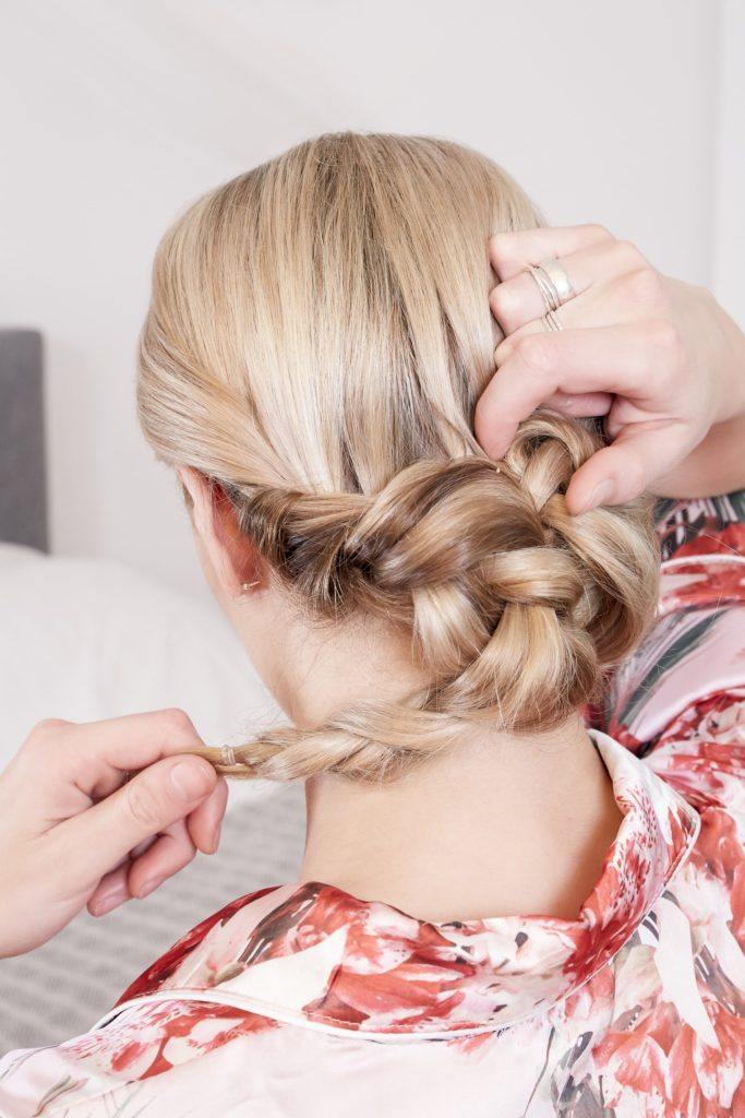 wedding chignon: back view of a blonde model wrapping her braided pigtails into a low chignon