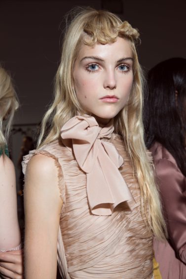 blonde model backstage at Rochas SS17 paris fashion week show wearing a dusty pink dress with a bow with long wavy hair with a curly fringe