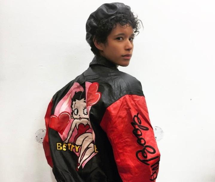 back shot of model with short curly hair wearing beret cap and biker jacket