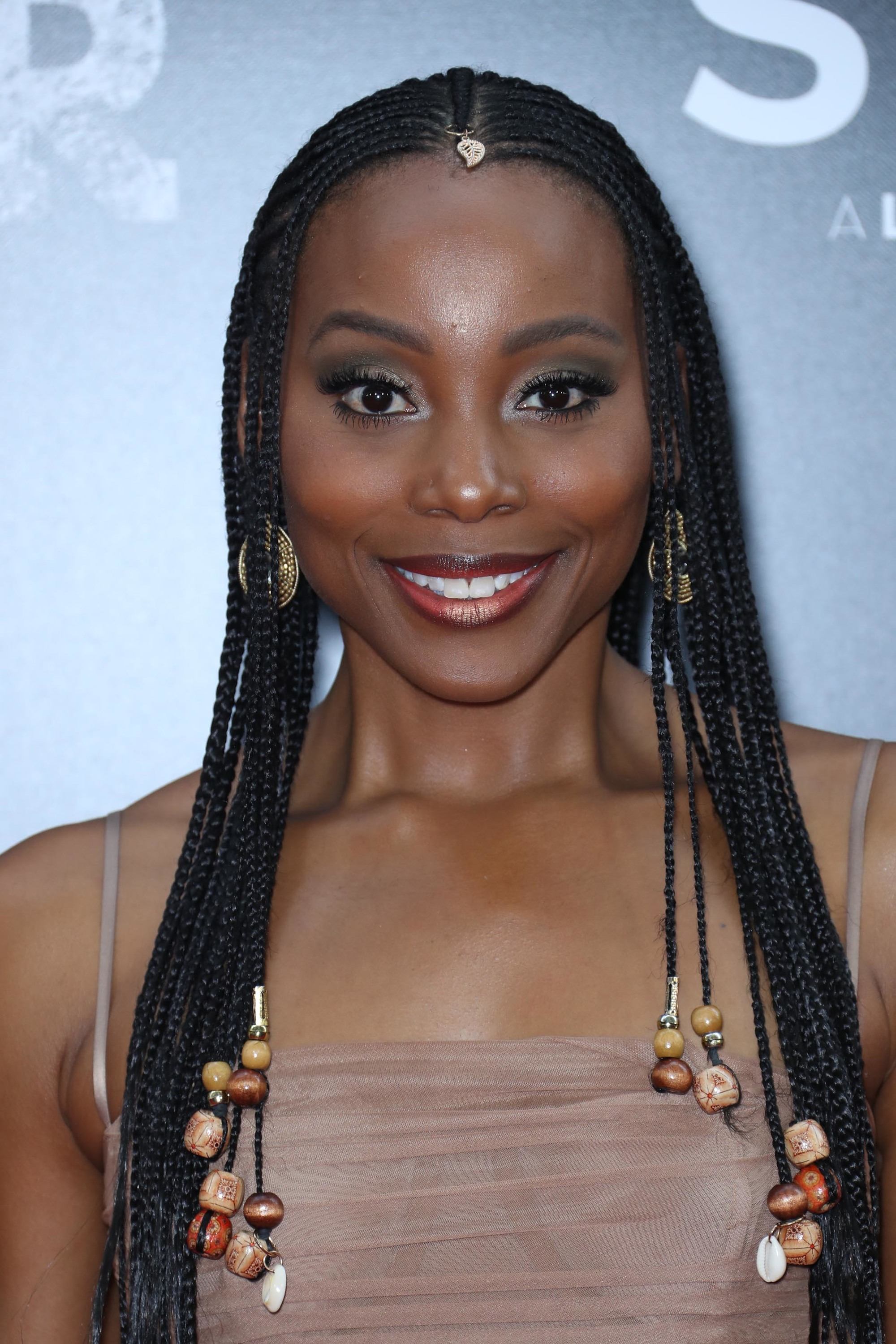 Black history month hairstyles: Close up shot of Erica Ash with dark brown cornrows with beads on the ends, wearing a brown top and posing on the red carpet