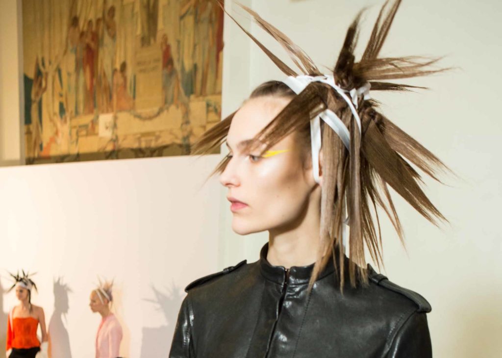 model backstage at the Haider Ackermann SS17 show with extreme spiky hair with a bandage wrapped around her head with a wing of colourful eyeliner