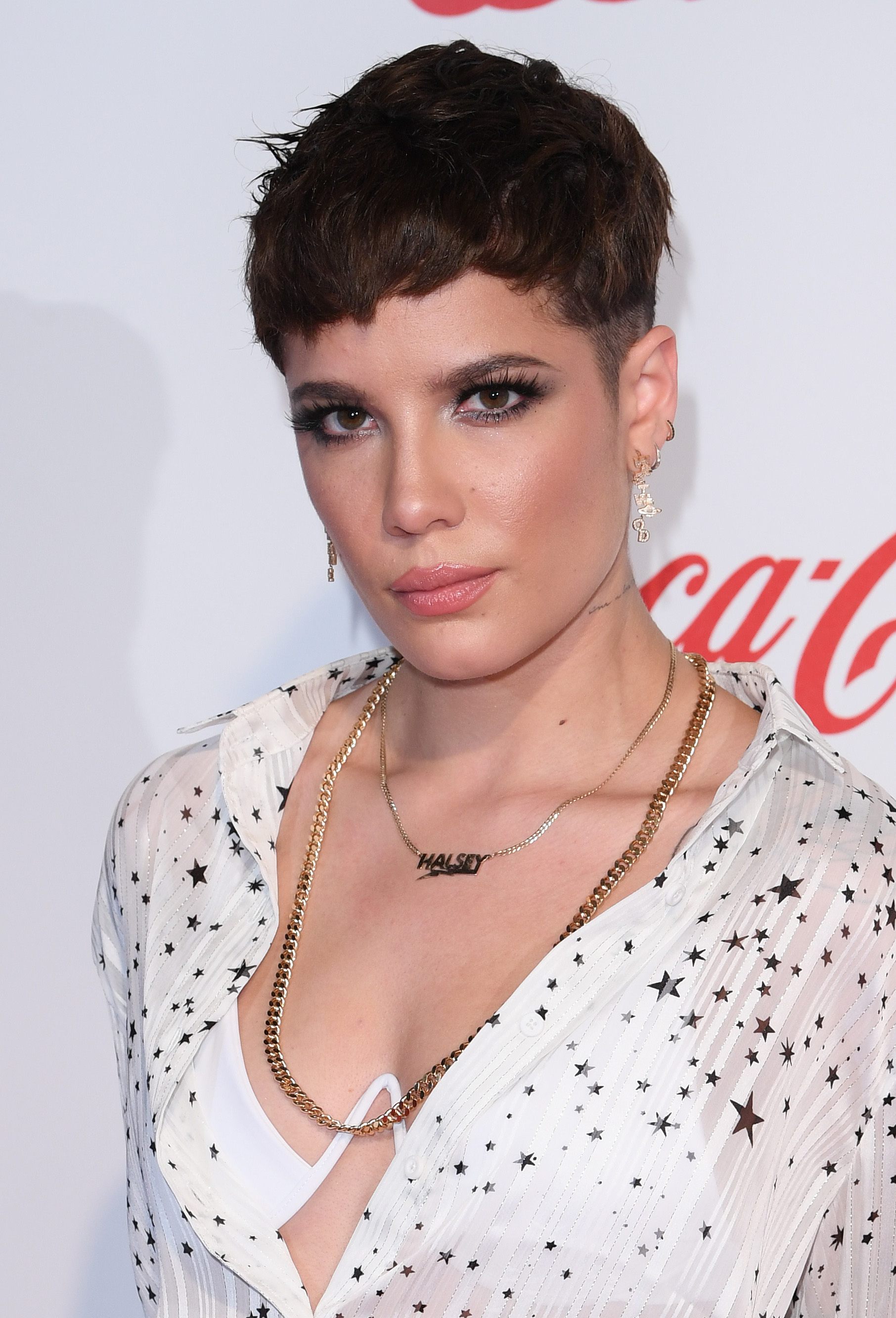 Haircuts for fine hair: Halsey with dark brown choppy pixie with low fade, wearing a white beaded dress with necklaces on the red carpet