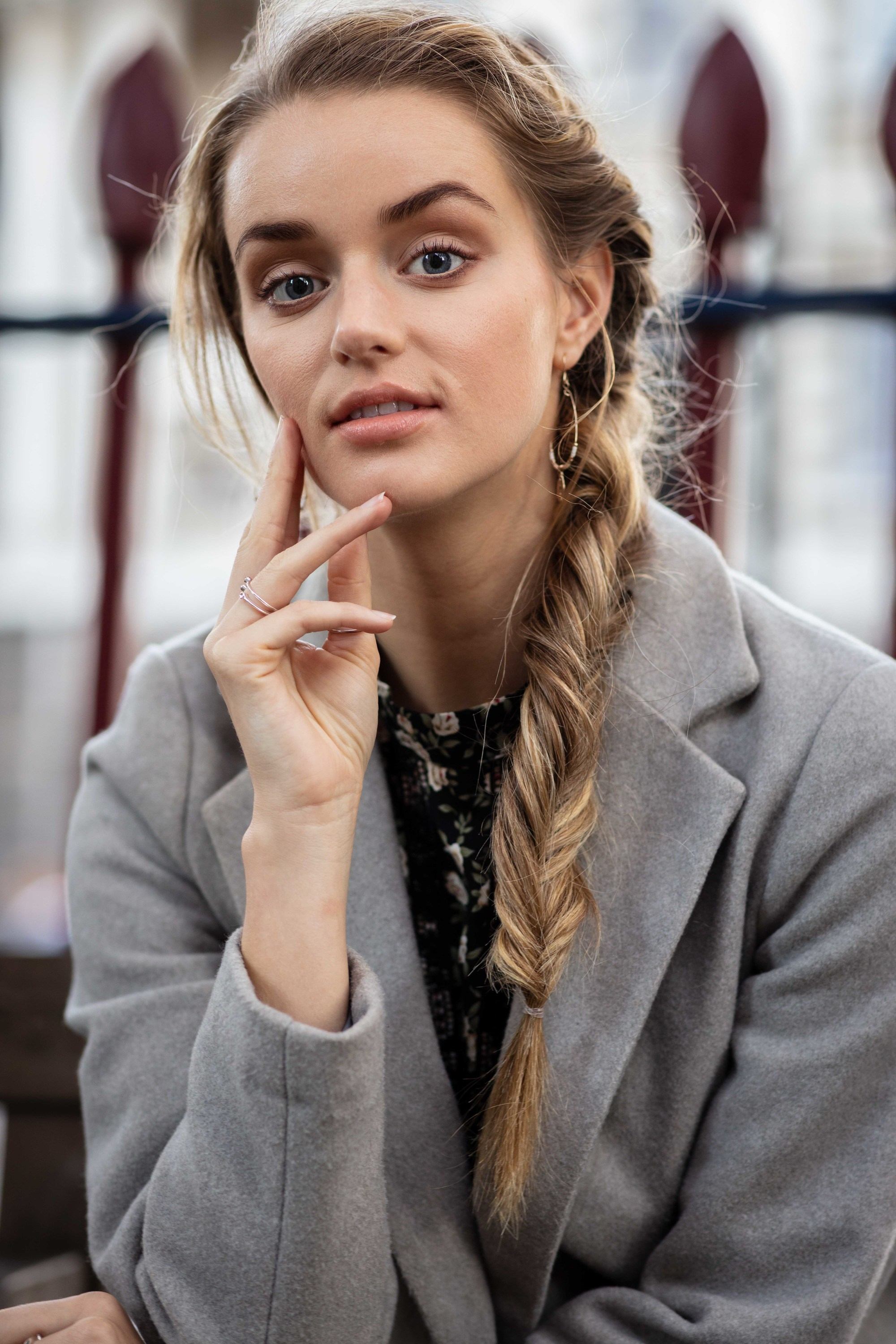 How to style long hair: Outdoor shot of a model with long blonde hair in a side fishtail braid, wearing a grey coat